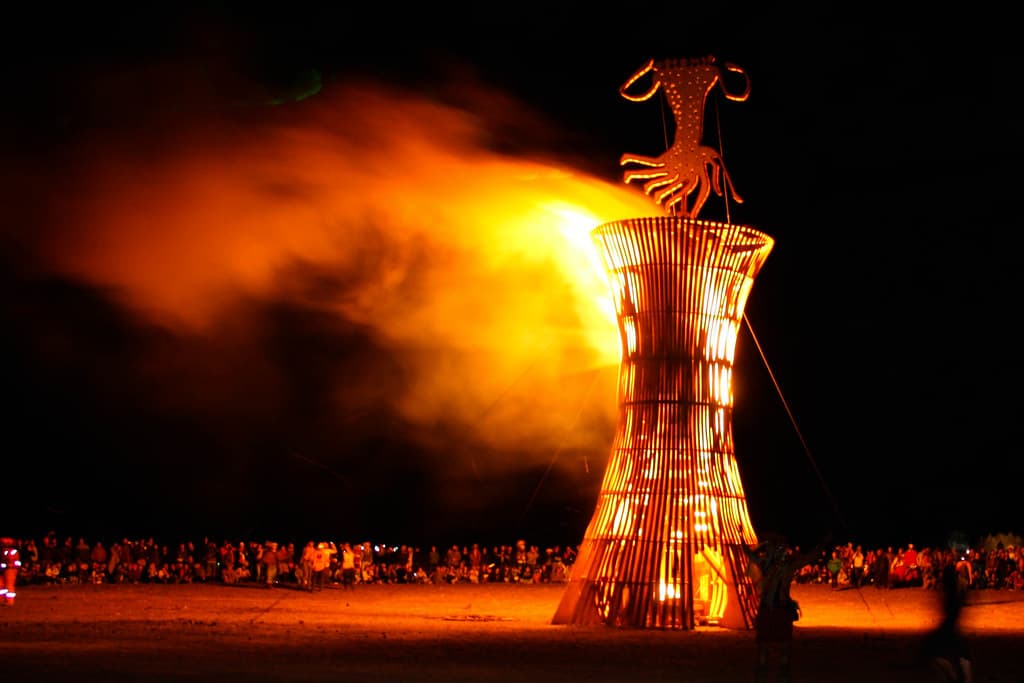 A tall wooden sculpture is engulfed in flames against the night sky at AfrikaBurn in the Tankwa Karoo