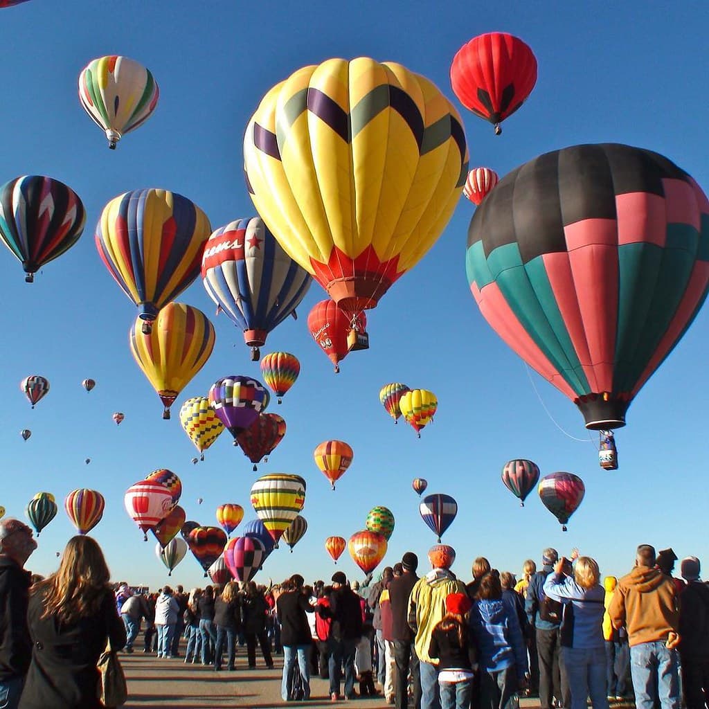 Dozens of colourful hot-air balloons rise into a blue sky above a crowd on the launch field at the Albuquerque International Balloon Fiesta