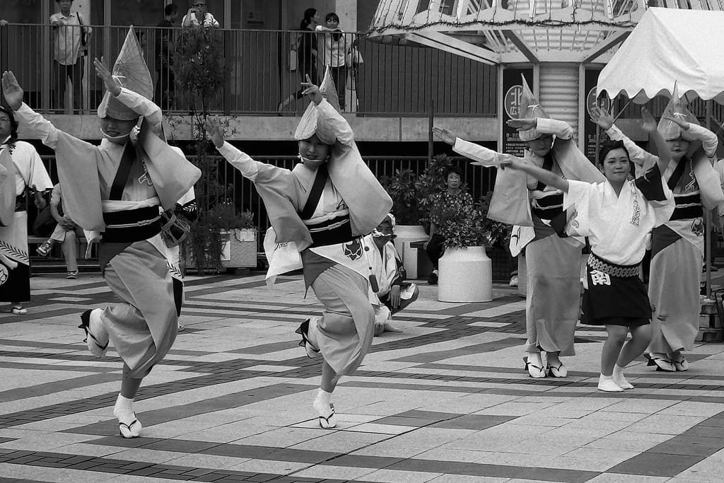 Dancers in traditional hats and happi coats performing Awa Odori in a black and white street scene