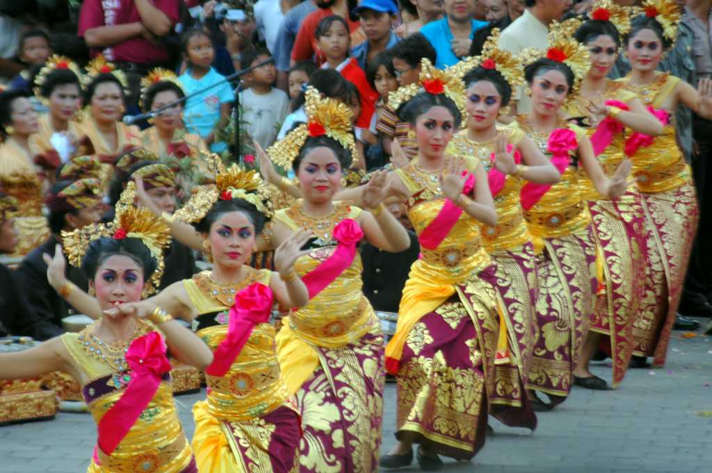 A long line of young Balinese dancers in gold and red costumes with flowered headdresses perform in the Bali Arts Festival parade