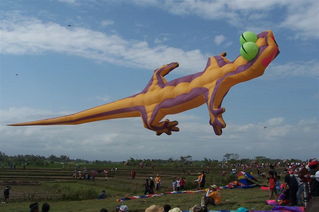 A giant lizard-shaped kite flying over the crowd at the Bali Kite Festival