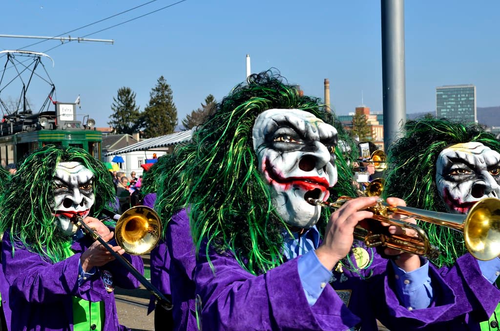 Fasnacht musicians in green-haired clown masks playing trumpets on a Basel street