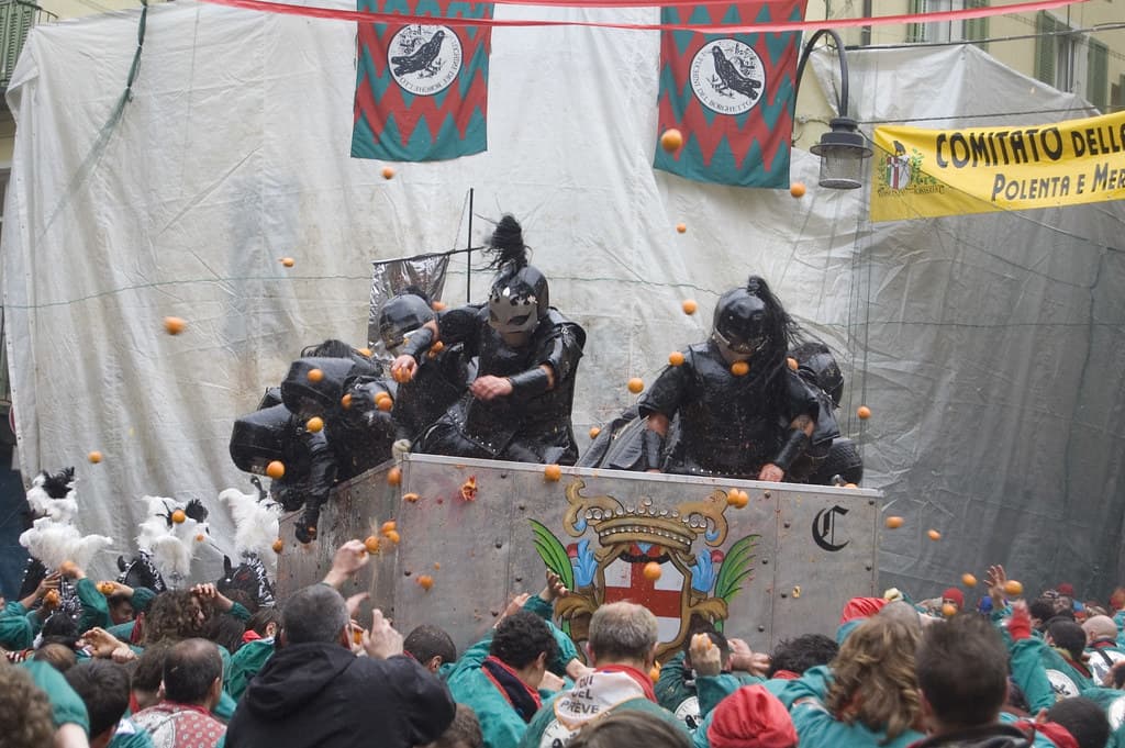 Masked throwers on a cart pelt a crowd of aranceri with oranges in a square in Ivrea