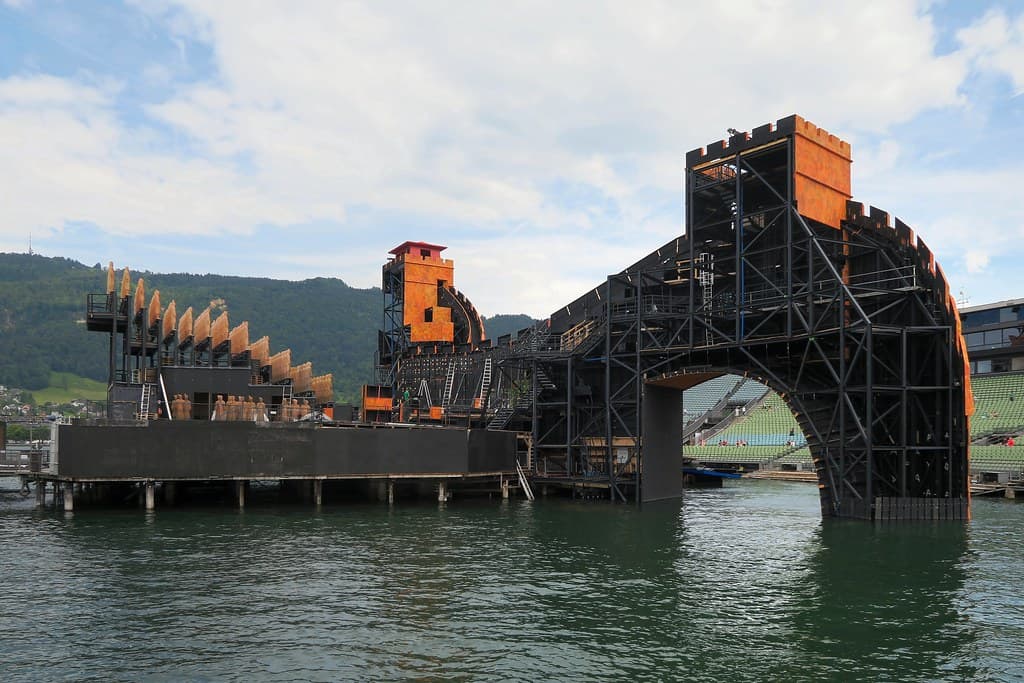 A giant stage set of a wall rises from Lake Constance behind the empty grandstand of the Bregenz lake stage