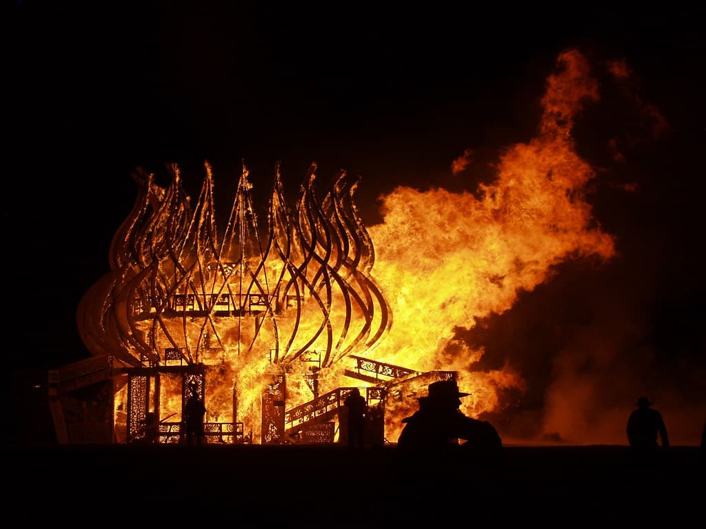 A wooden temple structure burns in towering flames against the night sky at Burning Man