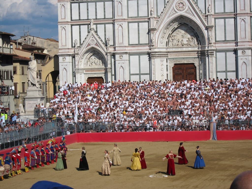 The costumed historic parade fills the sand pitch in Piazza Santa Croce before a calcio storico match, with packed stands and the basilica behind