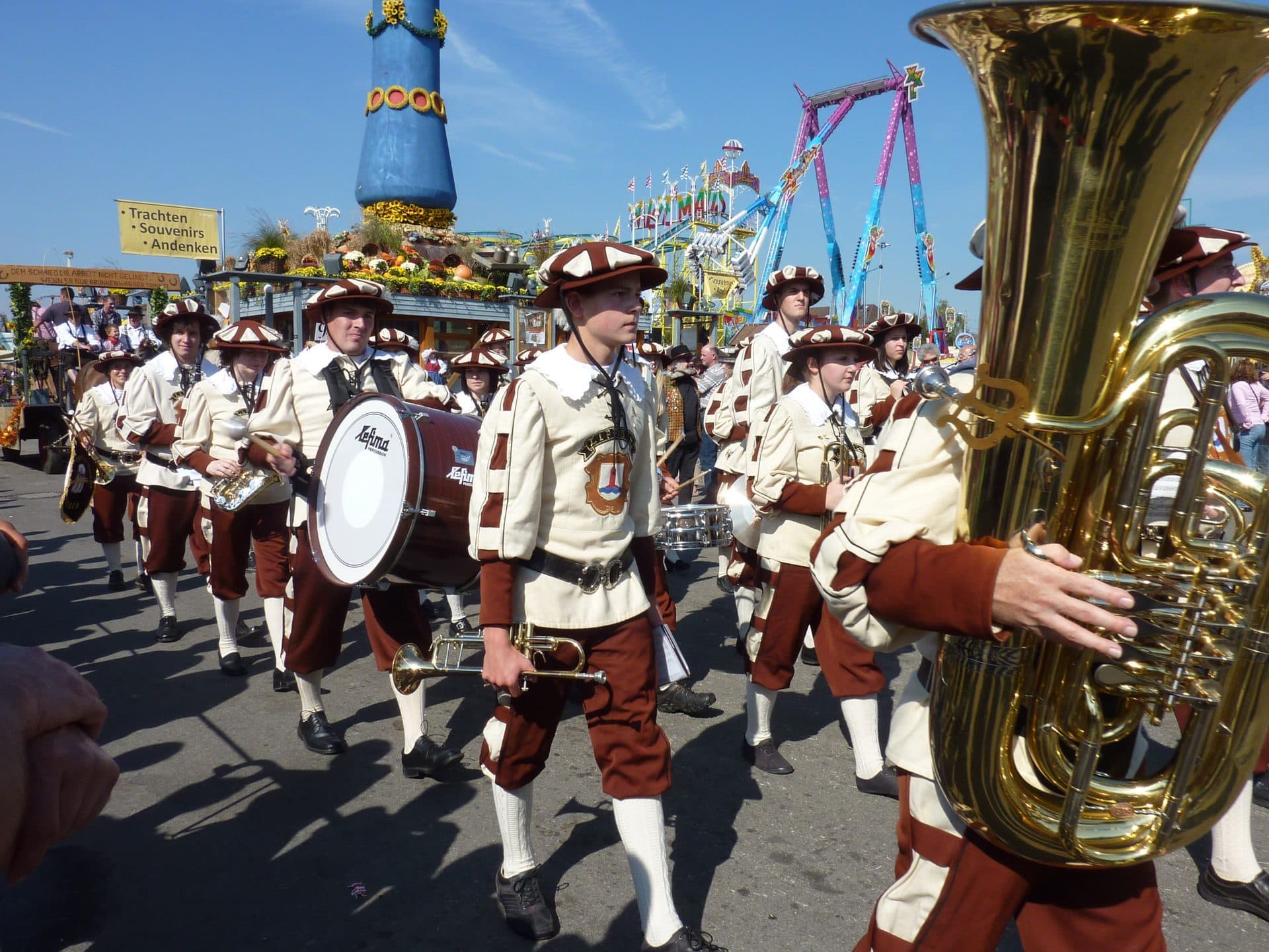A brass band in traditional costume marches past the Fruchtsäule at the Cannstatter Volksfest