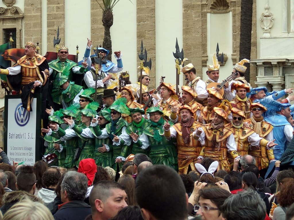 A carnival group in matching green and gold costumes performs for a crowd in a street of Cádiz