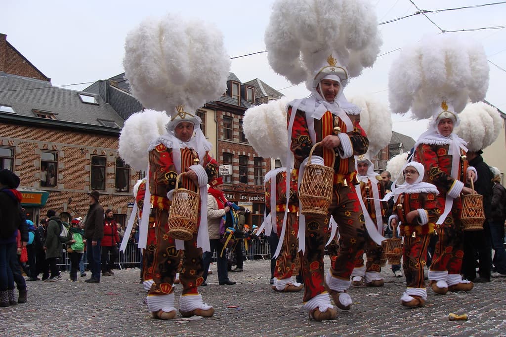 Gilles in towering white ostrich-feather hats and red, yellow and black costumes dance in a Binche square on Mardi Gras