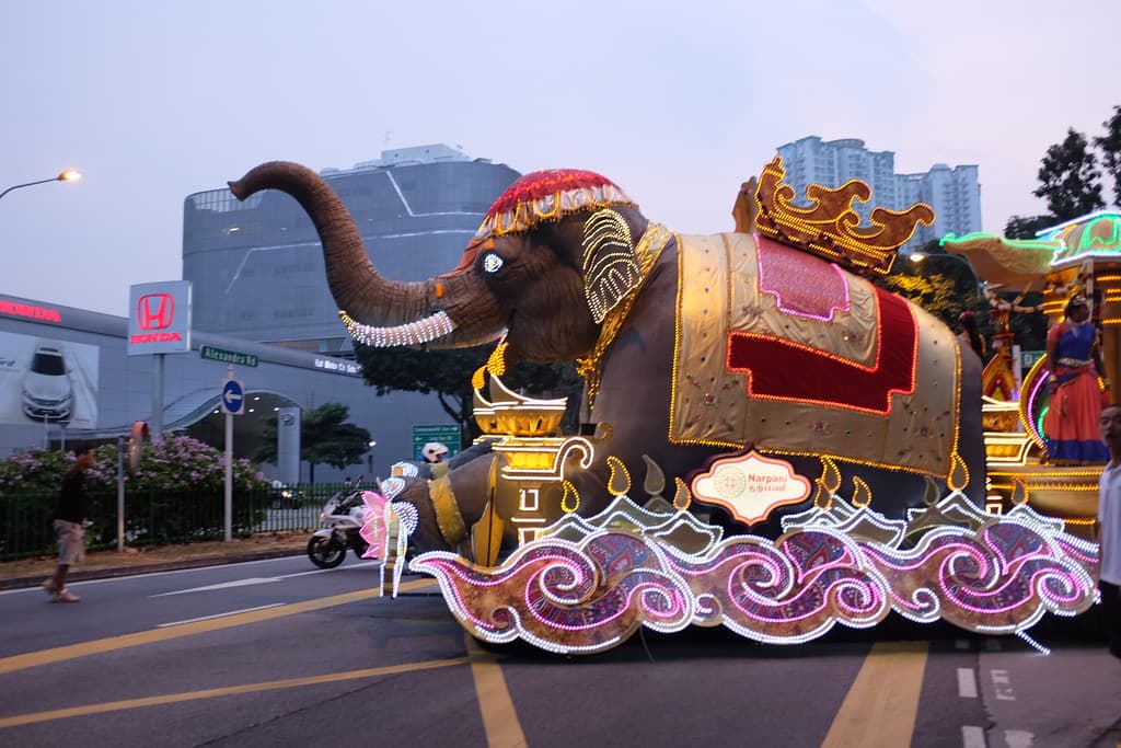 A giant elephant float decorated in gold and red rolls along a Singapore street at dusk during Chingay