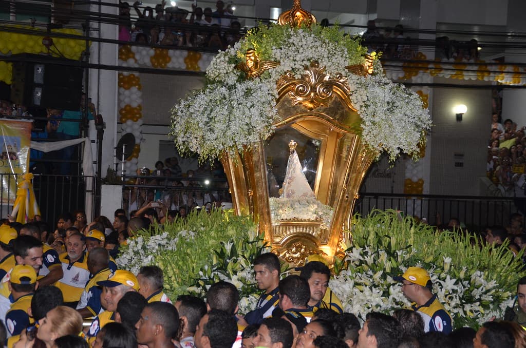 The golden, flower-decked carriage of Our Lady of Nazareth glows at night above a dense crowd of pilgrims in Belém