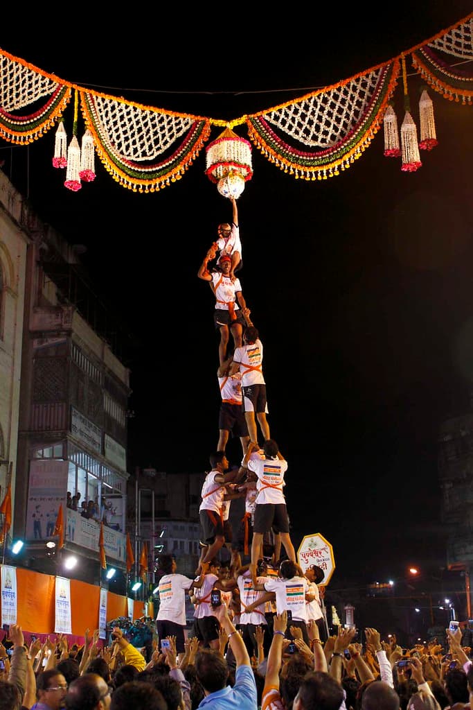 A tall human pyramid of Govinda climbers reaches a decorated pot at night during Dahi Handi in Mumbai