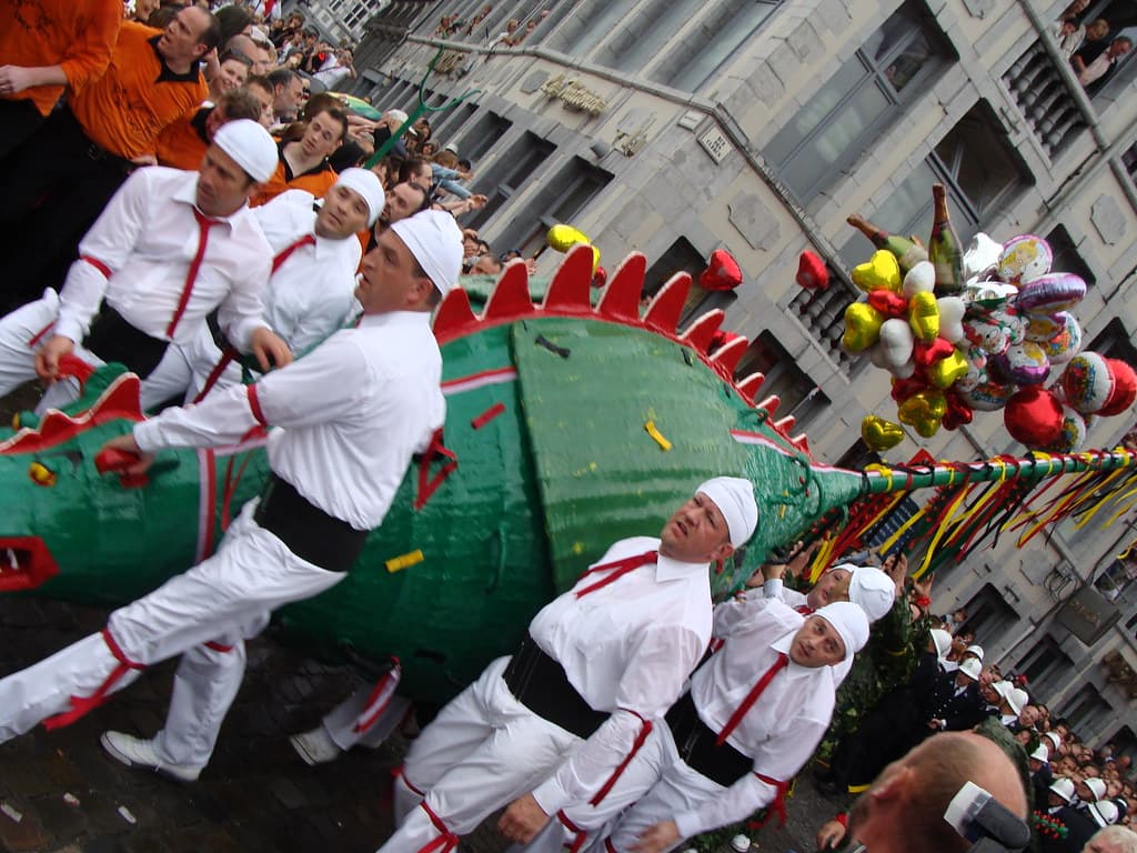 Men in white with red sashes carry the long green dragon through the crowd during the Lumeçon on the Grand-Place in Mons