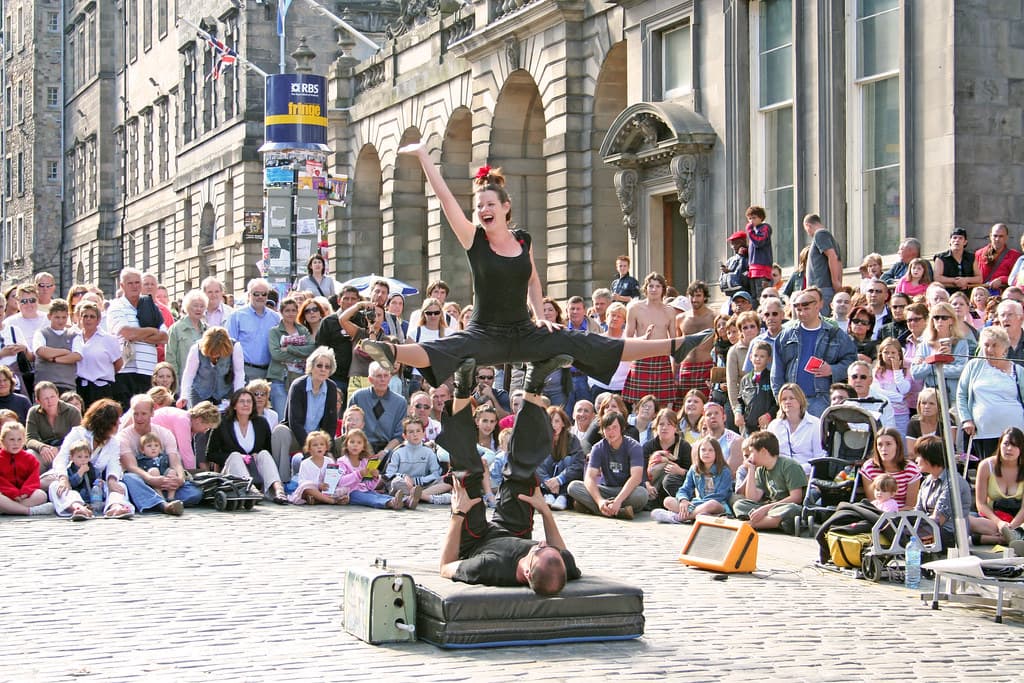 A circus strongman performs on the cobbles of Edinburgh's Royal Mile to a large seated crowd during the Fringe