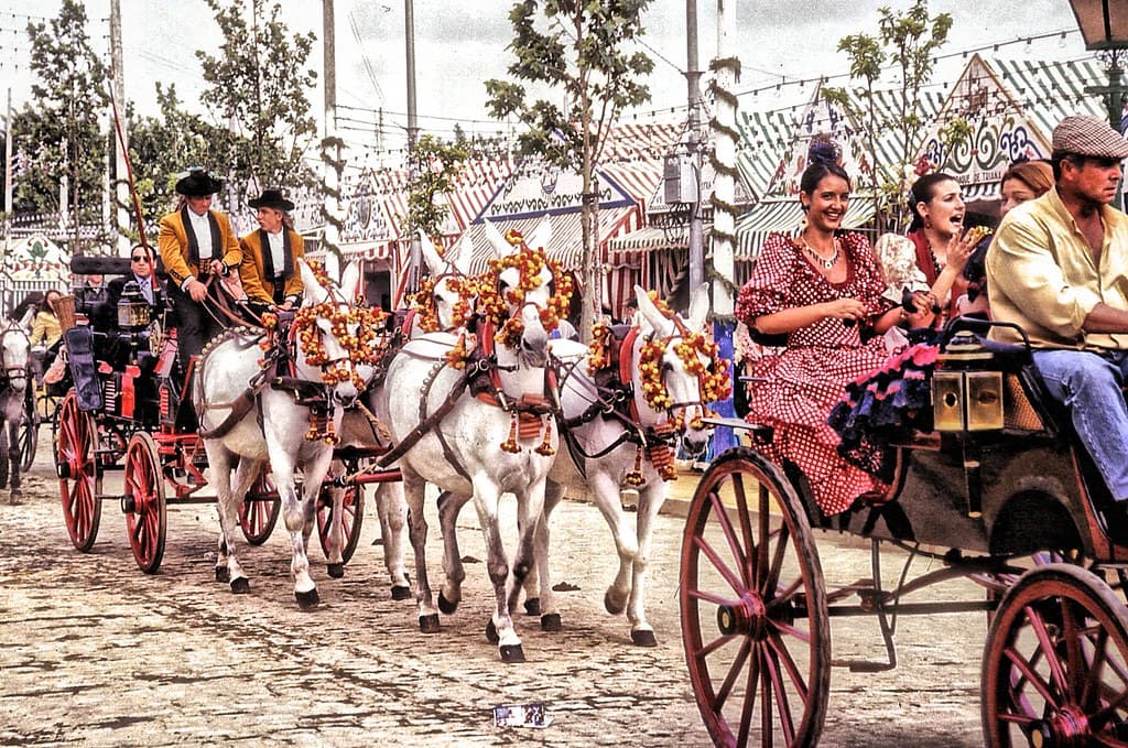 Horse-drawn carriages carrying riders in traditional dress at the Feria de Abril in Seville