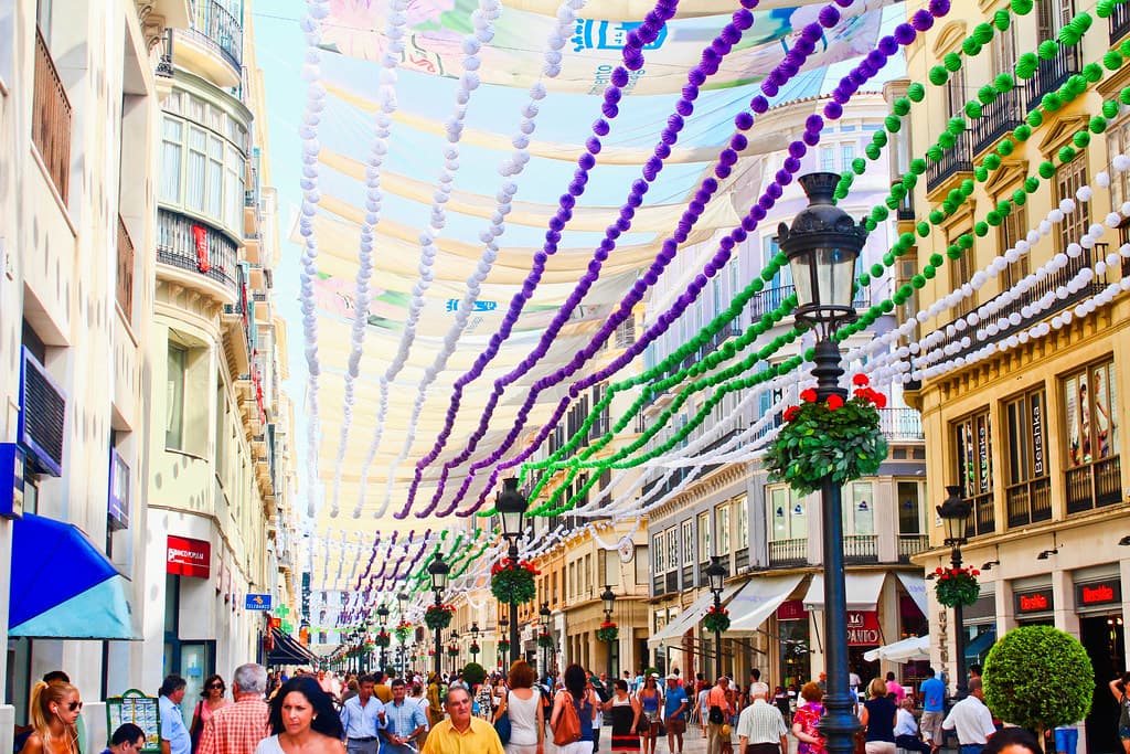 Crowds fill a street in central Málaga hung with colourful decorations during the August fair