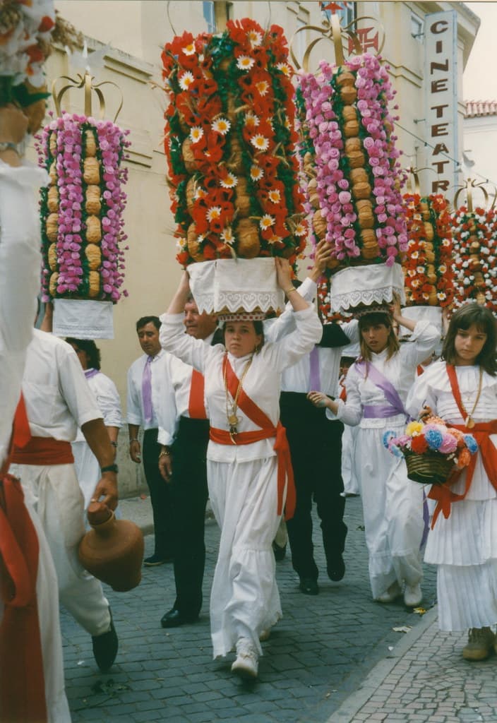 Women in white carry tall towers of bread decorated with colourful paper flowers on their heads in the Tabuleiros procession in Tomar