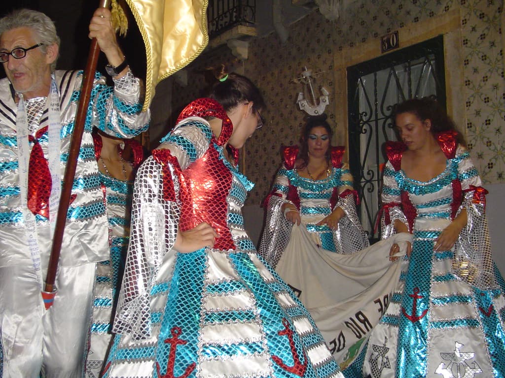 A marcha group in blue, white and red sequinned costumes dances with a decorated arch in a Lisbon street