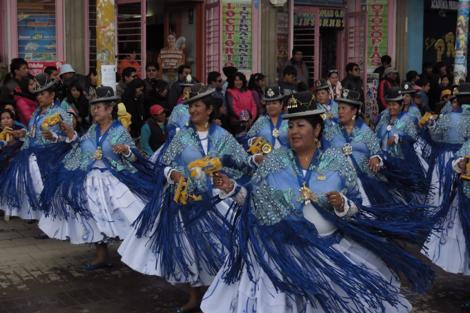 Dancers in blue skirts and bowler hats parade in formation through a crowded Puno street during the Fiesta de la Candelaria