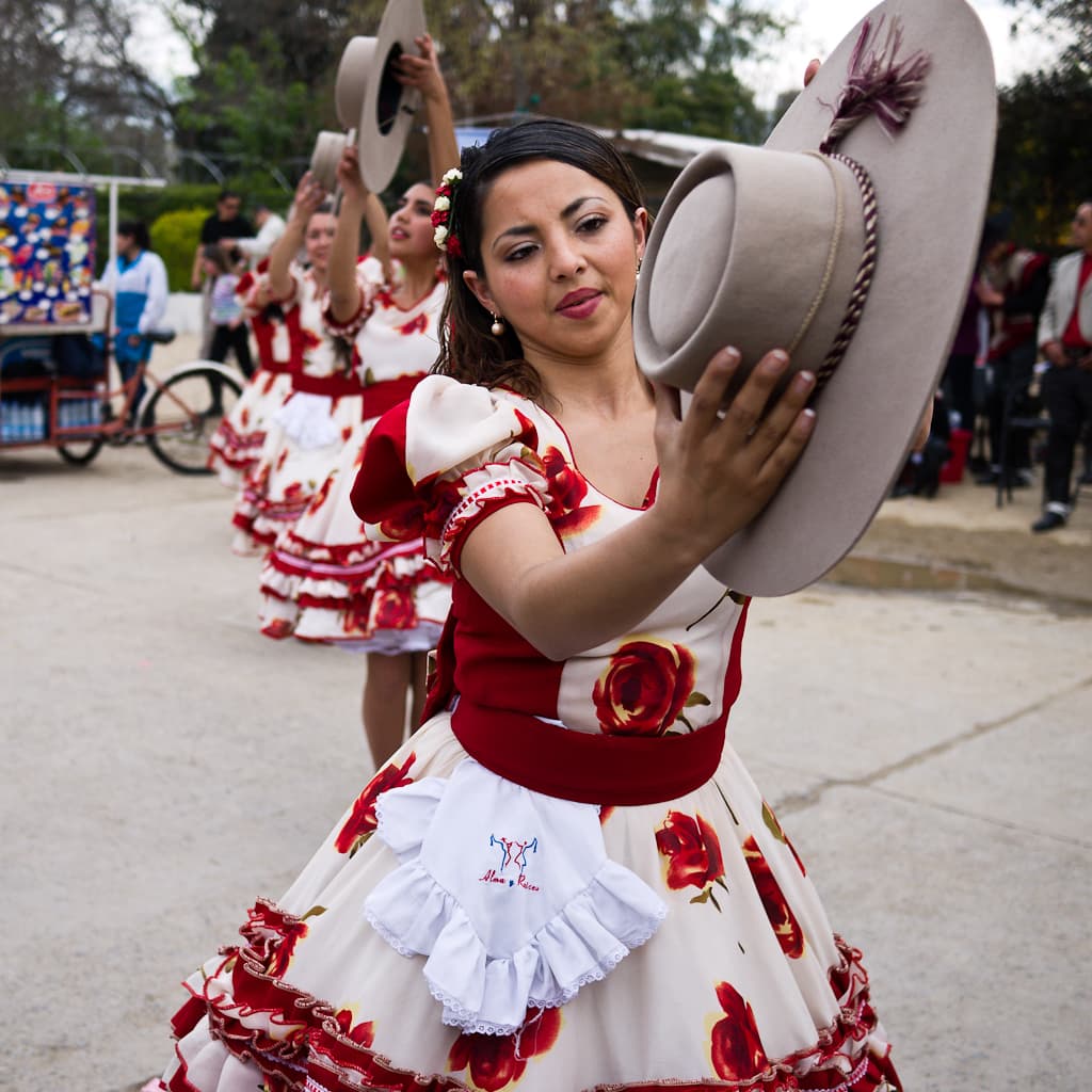 A cueca dancer in a red and white dress raises her hat during Fiestas Patrias in Santiago