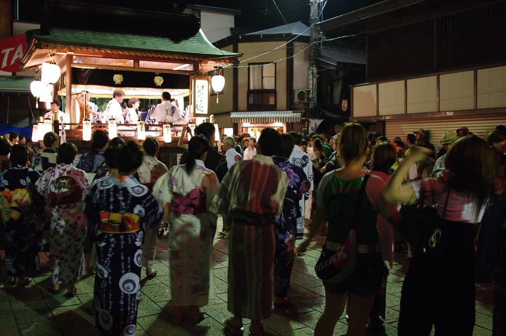 Dancers in yukata circle a lantern-lit musicians' float in a street of wooden houses in Gujo Hachiman at night