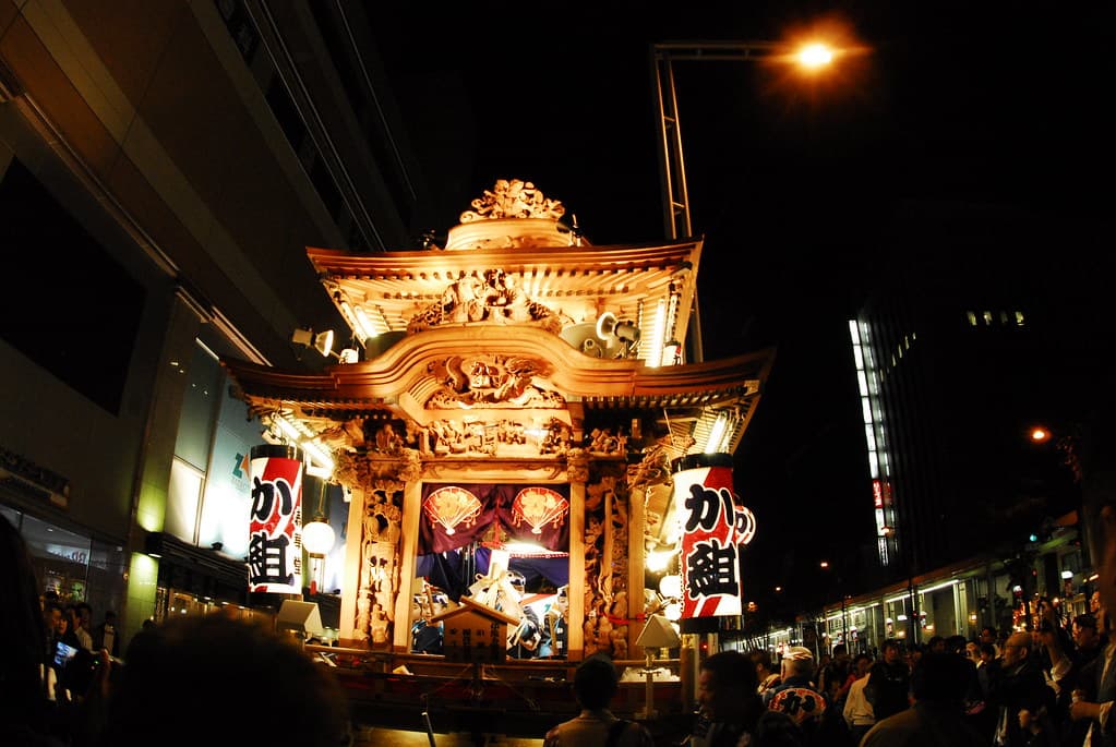 A carved palace float glowing with lanterns is pulled through central Hamamatsu at night during the festival