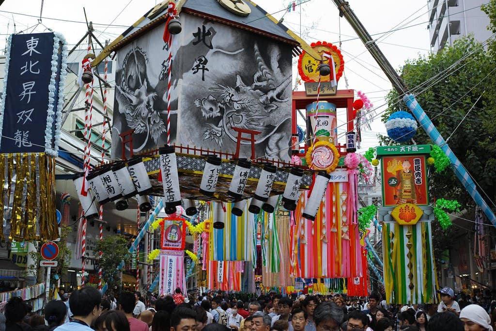 Giant Tanabata decorations with lanterns, streamers and painted panels hang over a packed street in Hiratsuka