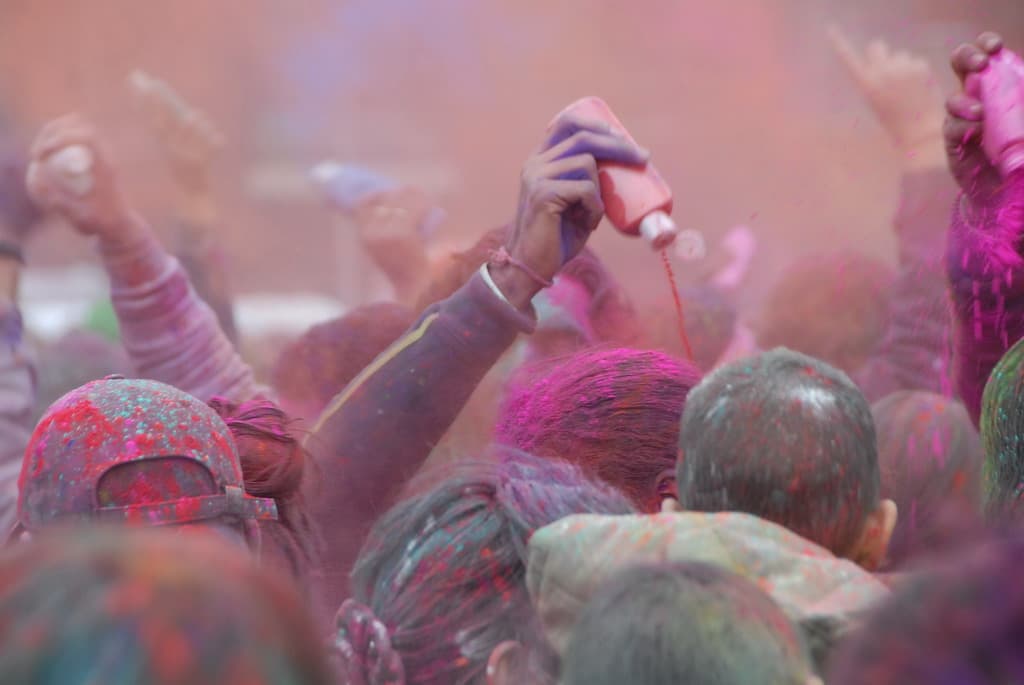 A crowd with raised hands covered in colored powder at Holi