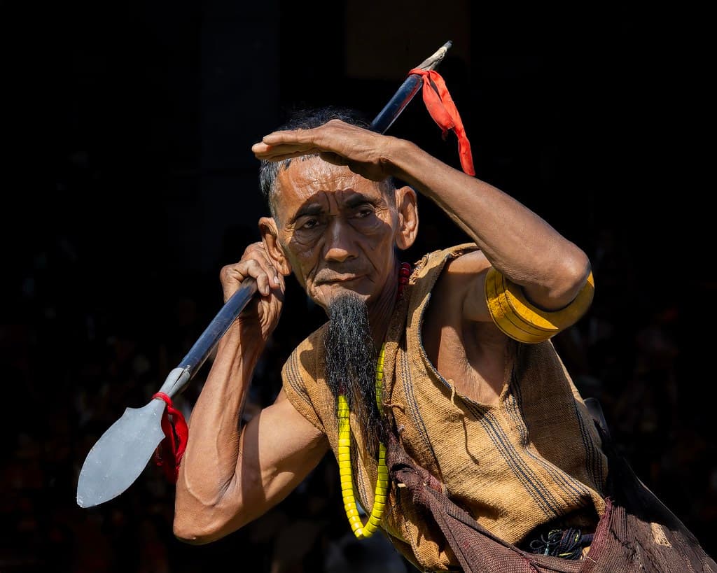A Naga man in traditional dress holding a spear, shielding his eyes, at the Hornbill Festival