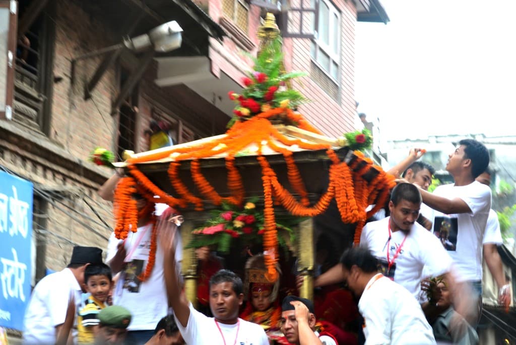 The Kumari sits in her chariot under an orange marigold canopy as men guide it through a Kathmandu street during Indra Jatra
