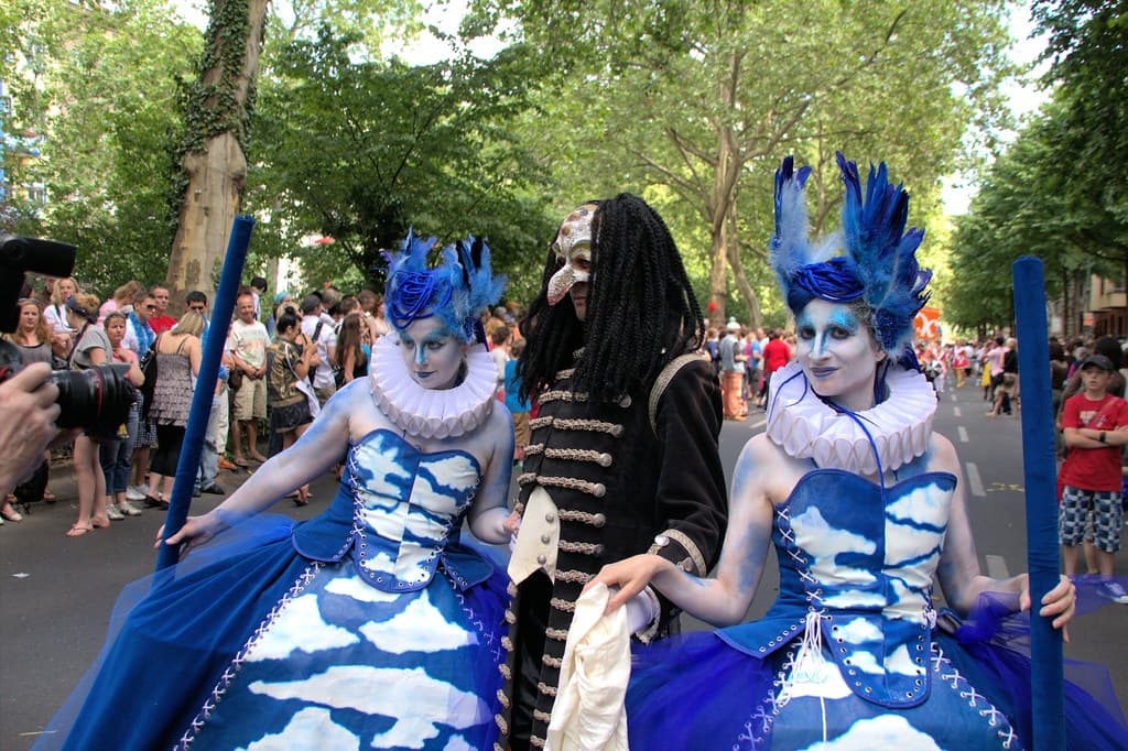 Dancers in blue and white costumes with tall headdresses parade at the Karneval der Kulturen in Berlin