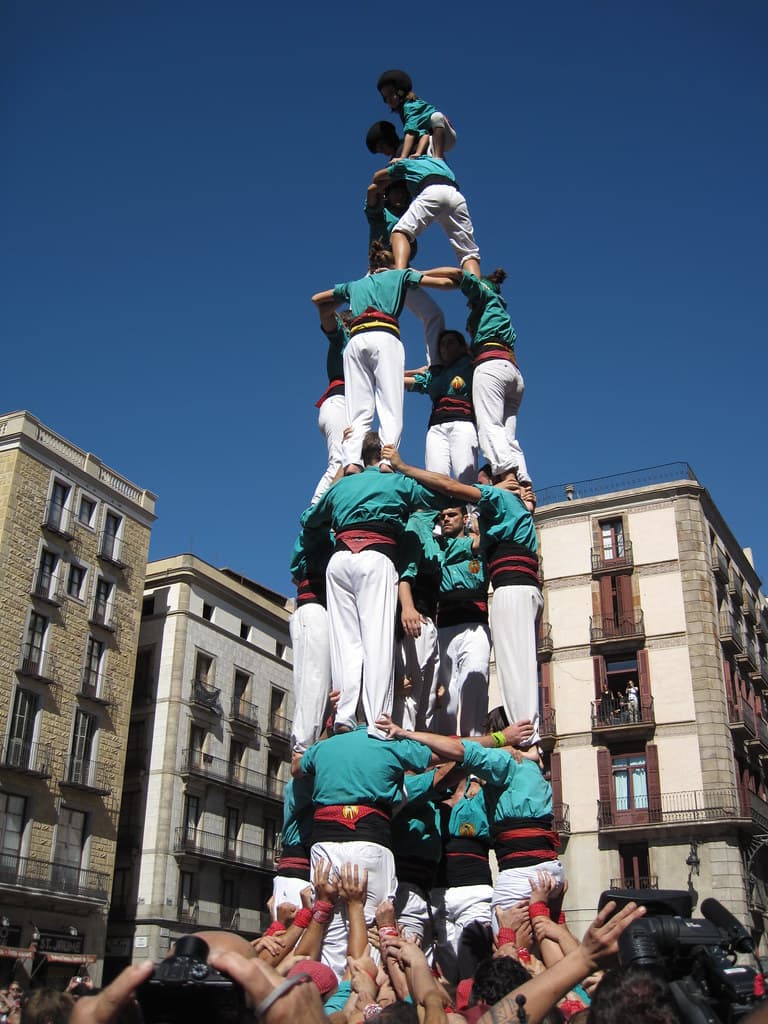 A tall human tower of castellers in green shirts rises above a packed crowd in front of Barcelona's city hall during La Mercè