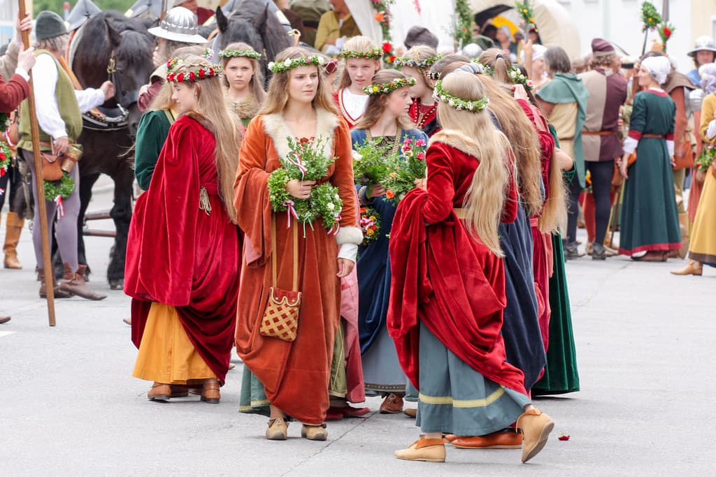 Women in long medieval gowns of red, green and gold carrying flowers walk in the Landshut Wedding procession
