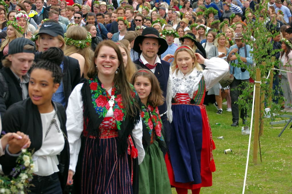 A crowd at Leksand's midsummer celebration, with women in Dalarna folk costume and flower wreaths in the foreground