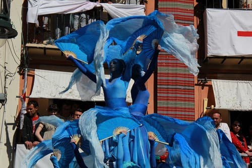 Festival participants in flowing blue costumes parade past balconies hung with red-cross banners in Alcoi