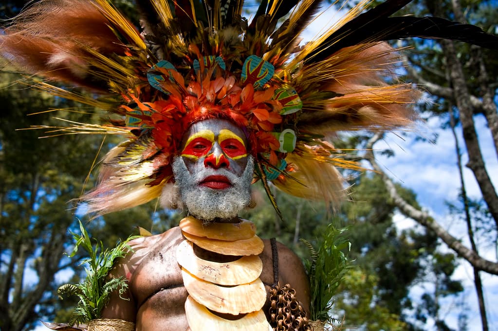 A highland performer in a huge headdress of red and orange feathers, with a painted face and shell necklace, at the Mount Hagen Show