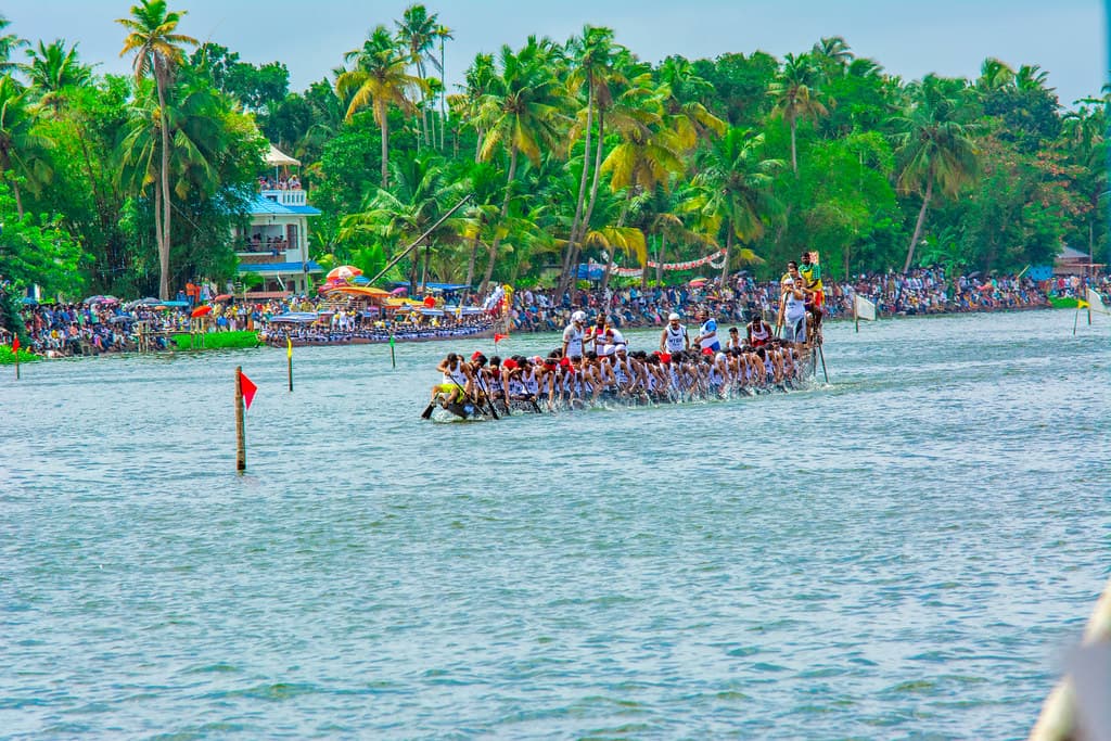 A long snake boat with its crew of rowers races down Punnamada Lake in front of crowded stands and palm trees