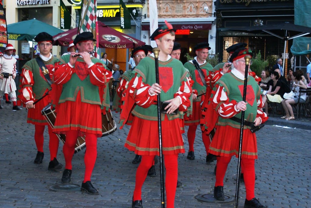 Men in red and green Renaissance costumes march on the cobblestones of the Grand-Place in Brussels during the Ommegang