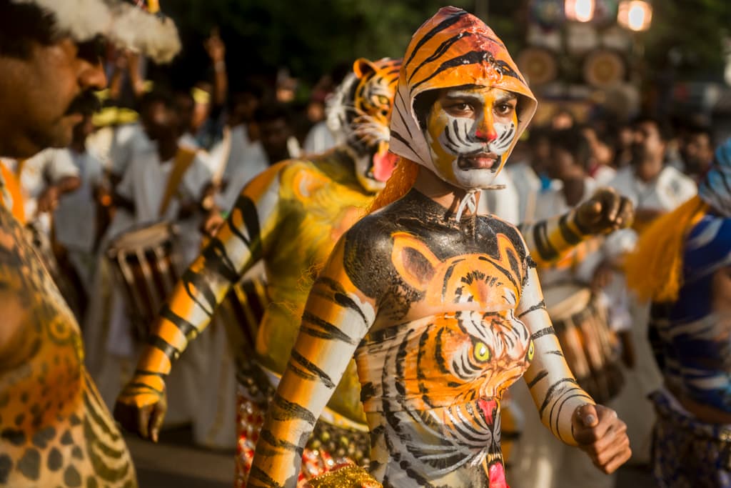 A pulikali tiger dancer in yellow and black body paint and a tiger mask performs in a Thrissur street