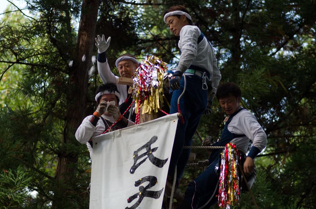 Men riding a sacred log in festival dress at the Onbashira Festival at Moriya Shrine
