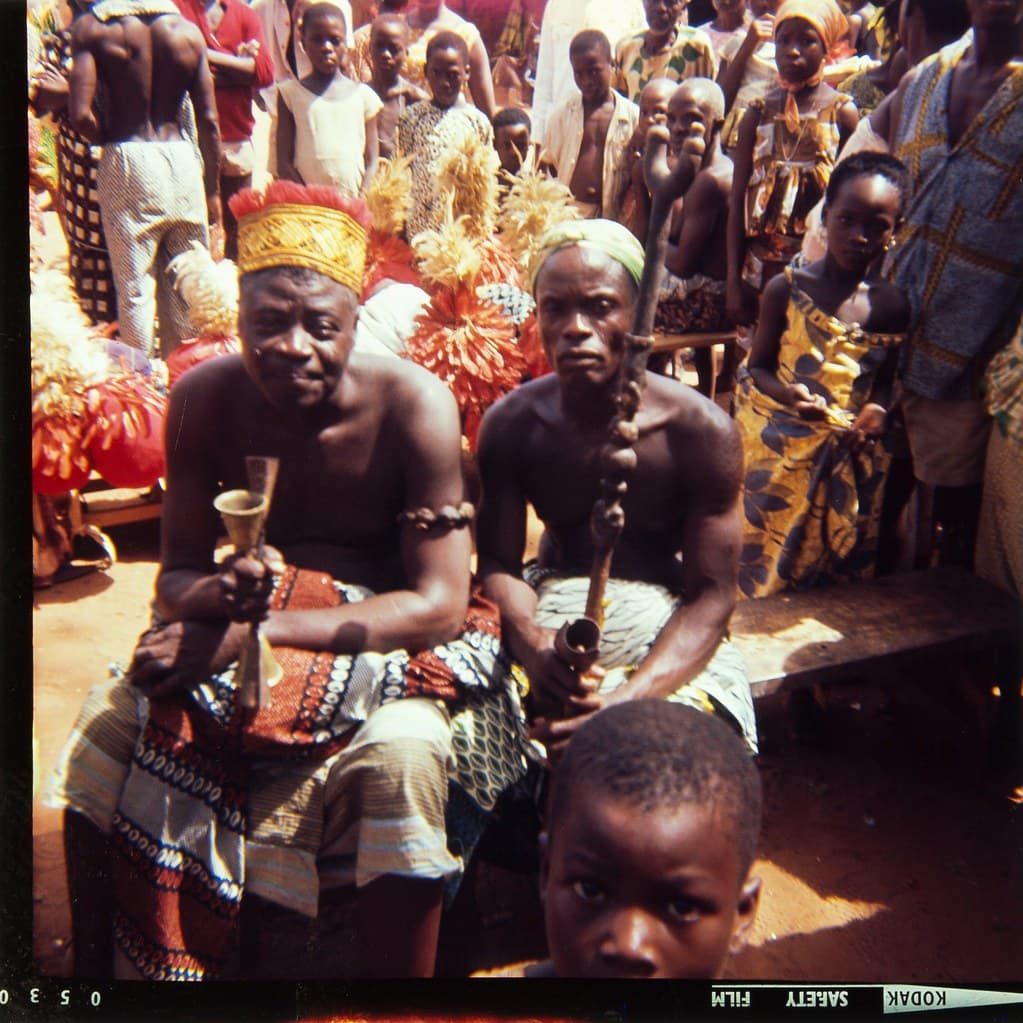 Two men in red ceremonial dress preparing for a vodun ritual in Ouidah