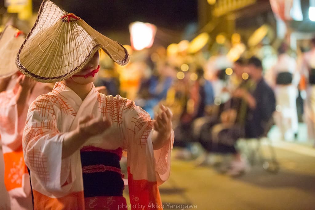 A dancer in a deep woven hat dancing through the night streets at Owara Kaze no Bon