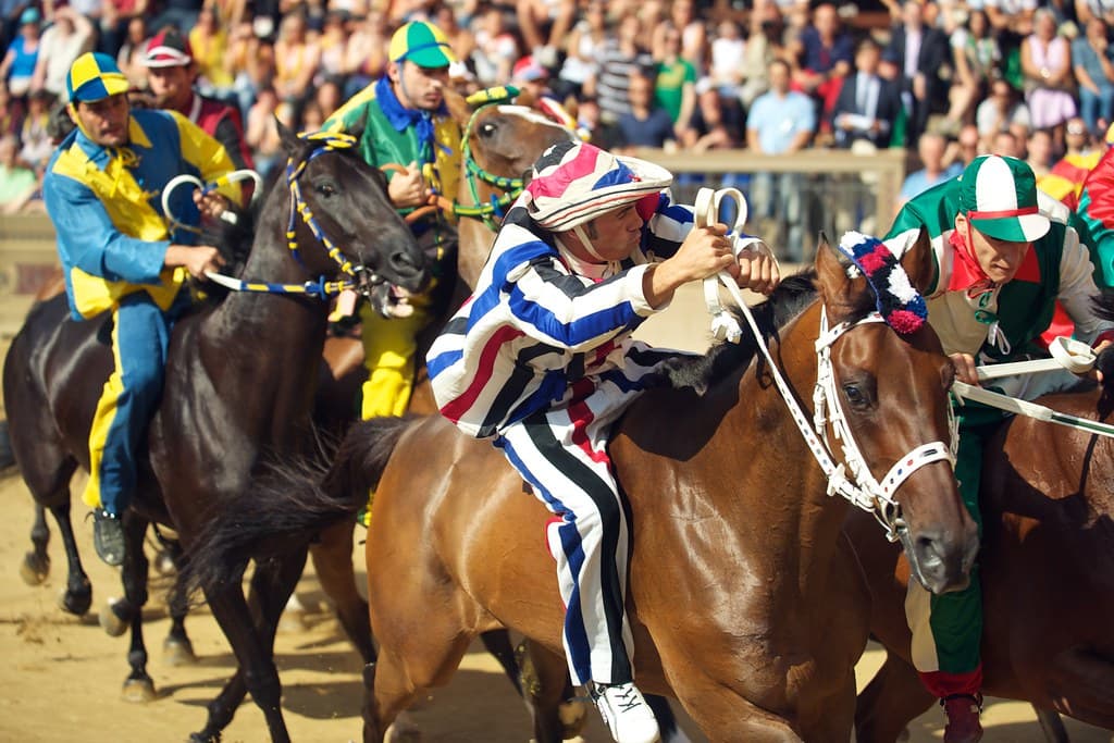 Jockeys in contrada colours ride bareback at the start of a trial run in Siena's Piazza del Campo, with packed stands behind