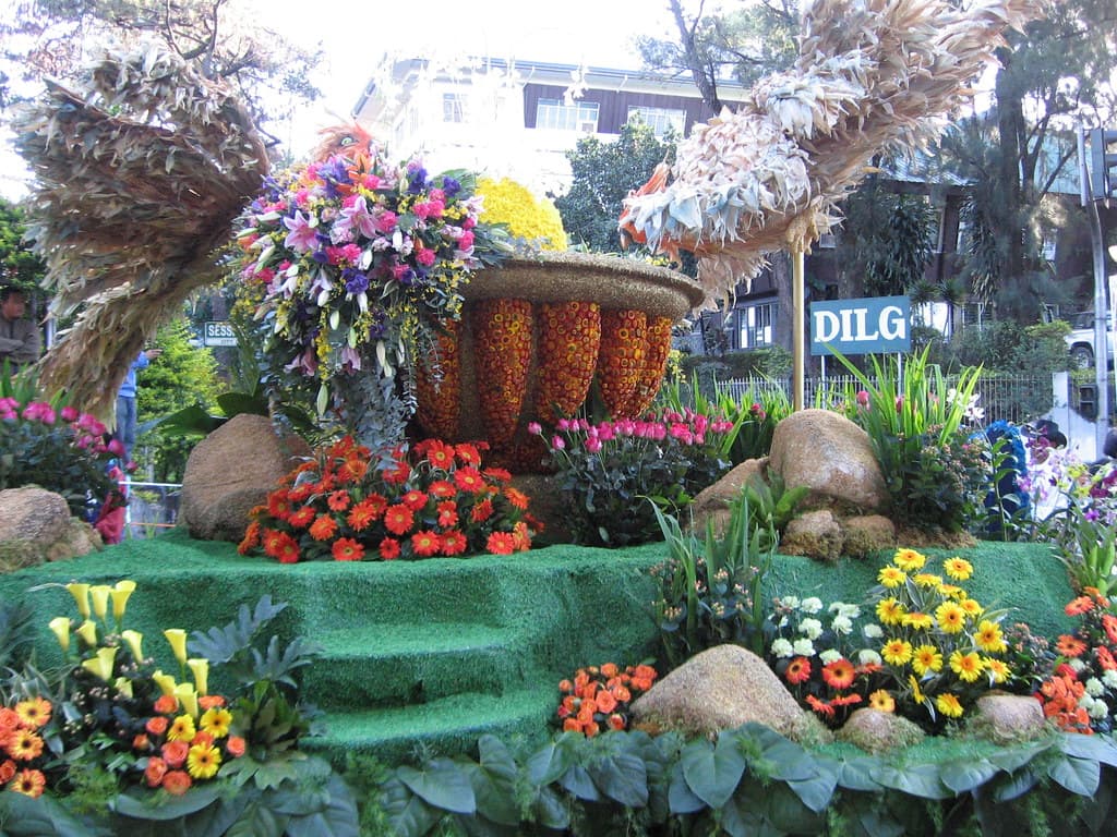 A parade float covered in flowers, with baskets and greenery, rolls along a street in Baguio during the Panagbenga float parade