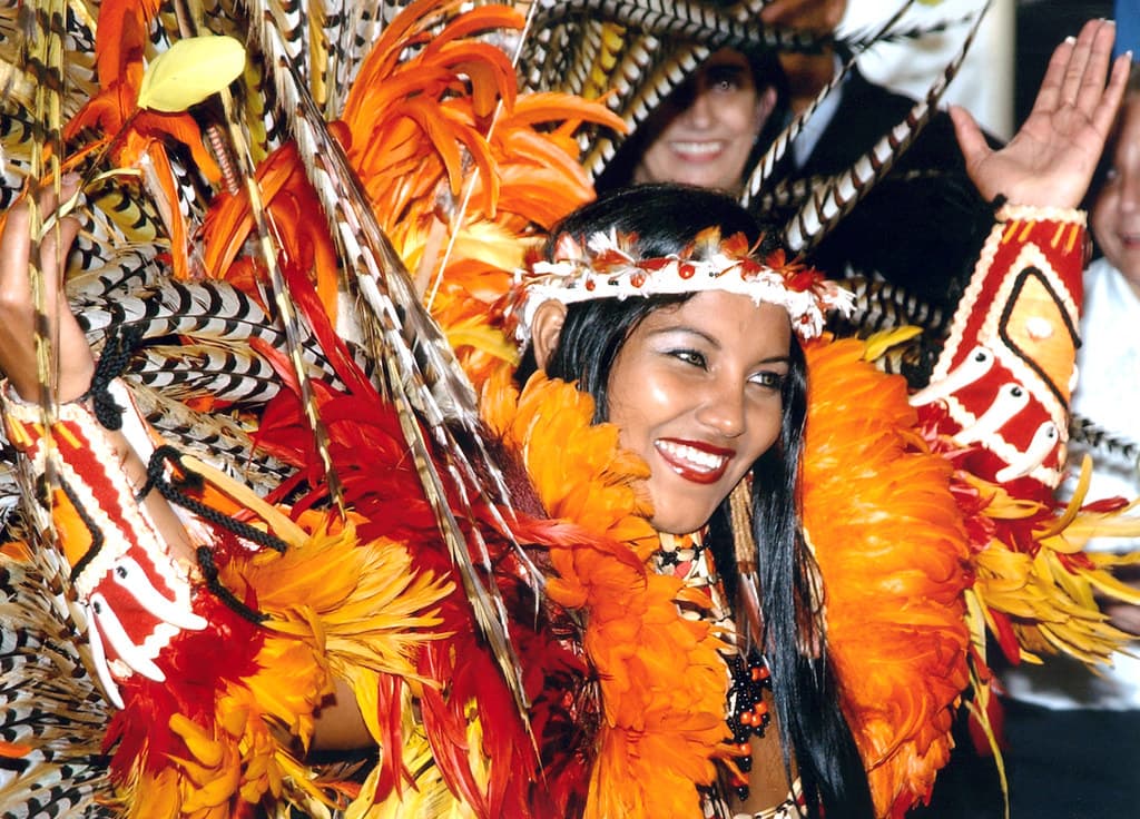 A smiling Boi Caprichoso dancer in a huge orange, red and feathered costume performs at the Parintins festival