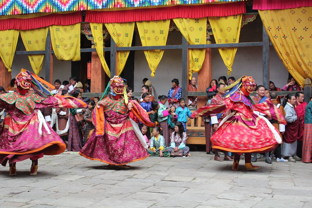 Masked dancers in red and pink costumes performing at a tshechu festival in Bhutan