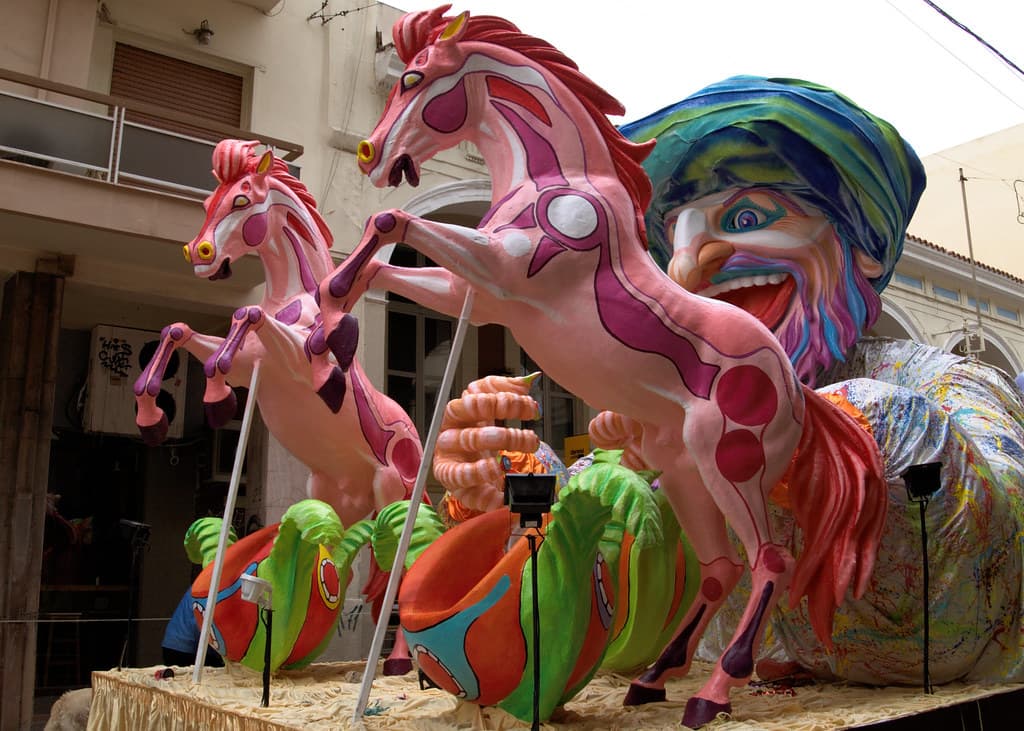 A colourful carnival float with giant rearing pink horses and a turbaned figure in a street in Patras