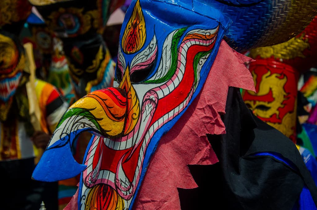 A brightly painted Phi Ta Khon ghost mask with a long curved nose in the crowd at a festival in Loei province