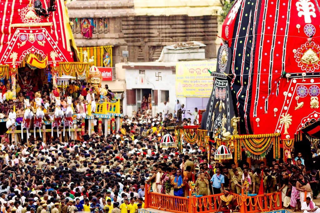 Towering temple chariots draped in red, yellow and black cloth rise above a vast crowd during Rath Yatra