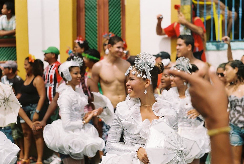 Carnival dancers in white costumes with feathered headdresses perform in a street in Olinda